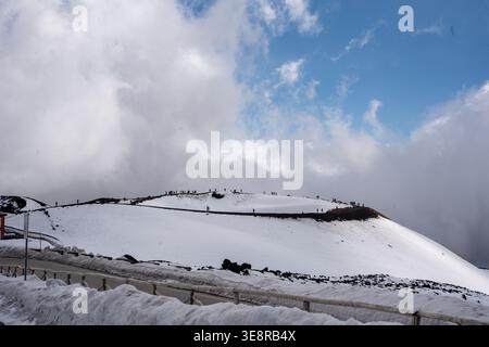 Blick auf eine schneebedeckte Landschaft unter einem bewölkten Himmel, mit Menschen auf einem entfernten Gipfel, die einen starken Kontrast zwischen weiß und Blau schaffen, Taormi Stockfoto