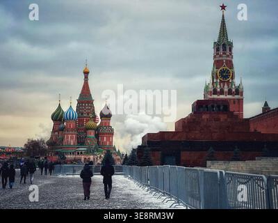 Menschen gehen auf dem Roten Platz mit Basilius-Kathedrale und Spasskaya-Turm des Kremls in Moskau, Russland. Winterszene mit Schnee und bewölktem Himmel Stockfoto