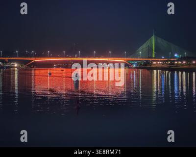 Nächtlicher Blick auf die Gazela-Brücke über die Save in Belgrad, Serbien, mit Stadtlichtern, die auf dem Wasser reflektieren. Stadtlandschaft und moderne Infrastruktur Stockfoto