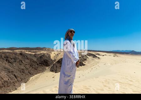 Ein arabischer Mann in Nationalkleidung steht in der Wüste Sinai oder Sahara und schaut auf den blauen Himmel. Mann in traditionellem Dschungdasha kandura und s Stockfoto