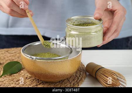 Frau, die Matcha-Pulver in eine Schüssel am weißen Holztisch siebt, Nahaufnahme Stockfoto