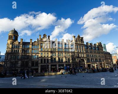 Manchester, Großbritannien - 28. Februar 2026: Historische Corn Exchange-Fassade in Manchester, Großbritannien mit Fußgängern, Sonnenlicht und dramatischem blauem Himmel. Stockfoto