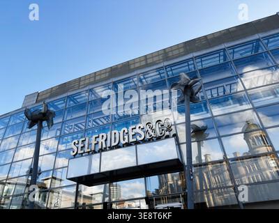 Manchester, Großbritannien - 28. Februar 2026: Große Glasfassade von Selfridges and Co in Manchester, Großbritannien, die historische Gebäude und den blauen Himmel reflektiert. Stockfoto