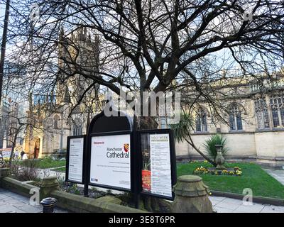 Manchester, Großbritannien - 28. Februar 2026: Blattloser Baum umrahmt die Begrüßungstafel und die gotische Fassade des Innenhof der Manchester Cathedral in Manchester, Großbritannien. Stockfoto