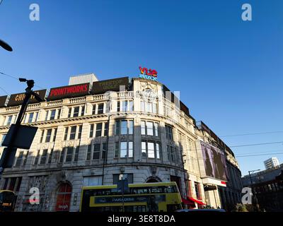 Manchester, Großbritannien - 28. Februar 2026: Sonnendurchflutetes, verziertes Geschäftsgebäude mit Kinowerbung, Bussen und städtischer Architektur in Manchester, Großbritannien. Stockfoto