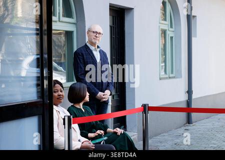 Verschiedene Kunden sitzen am frühen Morgen im Freien am Eingang des Bekleidungsgeschäfts und warten auf Black Friday-Angebote auf der Straße. Die Käufer reihten sich vor dem Einkaufszentrum an Stockfoto