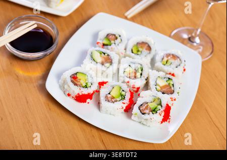 Sushi-Brötchen mit Lachs, Avocado und Gurke innen, Tobiko-Kaviar außen. Stockfoto