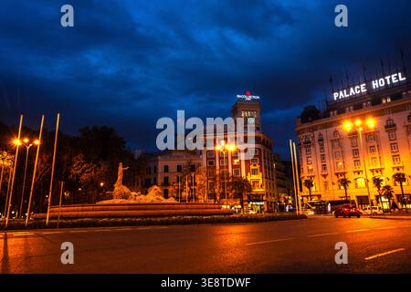 Madrids Fuente de Neptuno leuchtet in der Dämmerung, flankiert vom beleuchteten Palace Hotel und dem Paseo del Prado der NH Collection Madrid Stockfoto