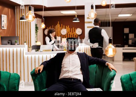 Geschäftsmann arbeitet mit vr-Headset in der Hotellobby und verwendet vor dem Einchecken eine neue interaktive 3D-Brille. Junger Erwachsener mit Virtual-Reality-Technologie auf Geschäftsreise. Stockfoto