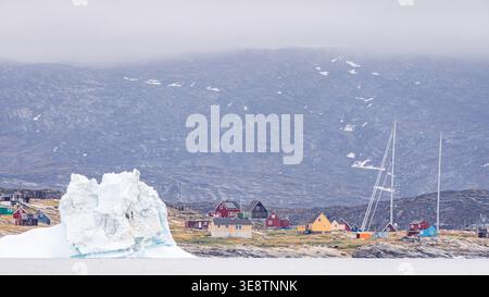 Grönländisches Dorf Saqqaq mit Eisberg, der vor der Küste schwimmt Stockfoto