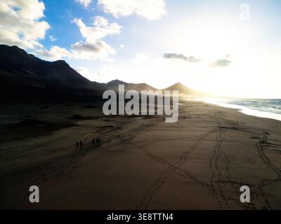 Blick aus der Vogelperspektive auf Playa del Confital mit Menschen, die auf dem Sand und den Bergen unter einer hellen Sonne in Las Palmas, Kanarischen Inseln, Spanien spazieren gehen. Stockfoto