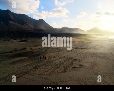Blick aus der Vogelperspektive auf Playa del Confital mit Menschen, die auf dem Sand in der Nähe zerklüfteter vulkanischer Berge unter hellem Himmel in Las Palmas, Kanarischen Inseln, Spa spazieren gehen Stockfoto
