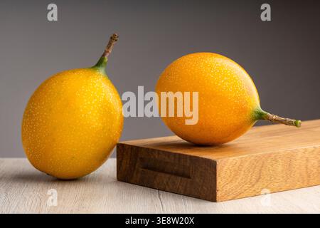 Frische granadilla-Früchte (Passiflora ligularis) auf Holzoberfläche, minimalistische Komposition mit neutralem Hintergrund. Stockfoto