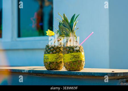 Hollywood, Florida, USA - 27. März 2026: Zwei geschnittene Ananas, die als Cocktailgläser verwendet werden, stehen draußen auf einem Holzvorsprung unter Sonnenlicht. Stockfoto