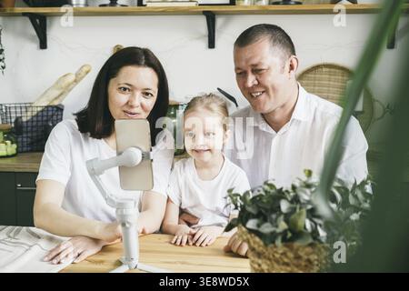 Familienspaß bei Familienanrufen. Mom, Dad und Tochter, die vier Jahre alt sind, lächeln glücklich und schauen sich den Bildschirm an. Das Konzept der Zeitvergabe t Stockfoto