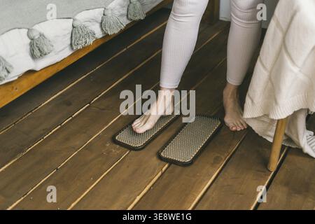 Nahaufnahme von menschlichen Beinen, die mit Nägeln auf einem Yoga-Brett aufstehen. Eine Frau übt, auf Nägeln zu stehen. Verbesserung des Körpers und Pflege des Körpers mit Stockfoto
