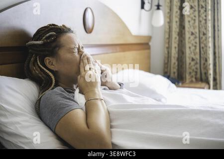 Die Frau liegt im Bett mit einem Taschentuch an die Nase gepresst. Das Mädchen ist kalt und niest schwer. Die Person hat Grippe und ist in Bettruhe. Grippe und Erkältungssympto Stockfoto