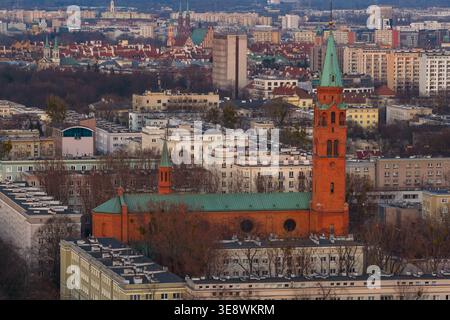 Blick aus der Vogelperspektive auf die historische Augustinerkirche mit ihrem hohen grünen Turm und der roten Backsteinfassade, umgeben von städtischen Wohngebäuden in Warschau, Stockfoto