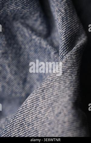 Blaue Denim-Jeans-Stoffstruktur – Nahaufnahme mit gefaltetem Makrodesign und weichem, unscharfem Hintergrund Stockfoto