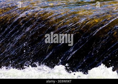 Wasserblätter über dunklem Felsen, während die Spritzer unter das Sonnenlicht steigen und feine Details einfangen, um Bewegungsreinheit und natürliche Energie zu veranschaulichen, die perfekt für Öko sind Stockfoto