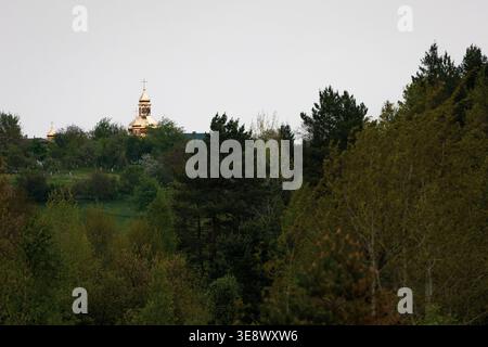 Goldene Kirchtürme erheben sich an einem ruhigen Frühlingsmorgen unter einem hellen Himmel über dichten Wald. Ferne Architektur leuchtet durch die Bäume, die entstehen Stockfoto