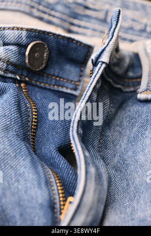 Blaue Denim-Jeans mit Messing-Reißverschluss und Knöpfen – Makronaht mit gezerknitterter Stoffstruktur und weichem, unscharfem Hintergrund Stockfoto