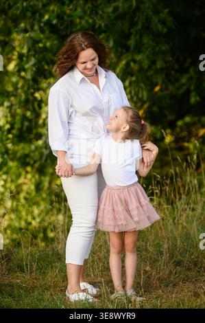 Glückliche, reife Mutter und Tochter verbringen Zeit miteinander im Sommerpark, schauen sich gegenseitig an und umarmen sich. Das Konzept der Spätelternschaft, der Naturerholung, der Liebe. Mutter-Tochter-Beziehung Stockfoto