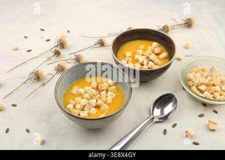 Kürbiscremesuppe und Brotcroutons. Kürbissuppe im Herbst oder Winter auf dem Tisch mit getrockneten Blüten. Stockfoto