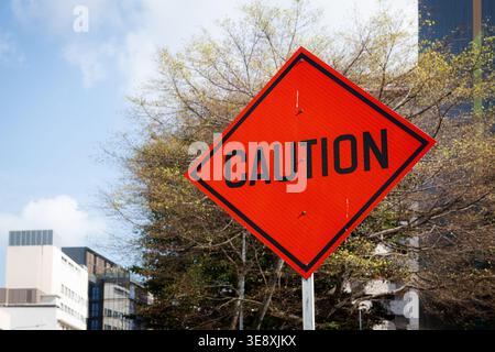 Helles, orangefarbenes, diamantbesetztes Verkehrswarnschild, das den Autofahrer warnt, mit Vorsicht durch eine Baustelle zu fahren. Stockfoto