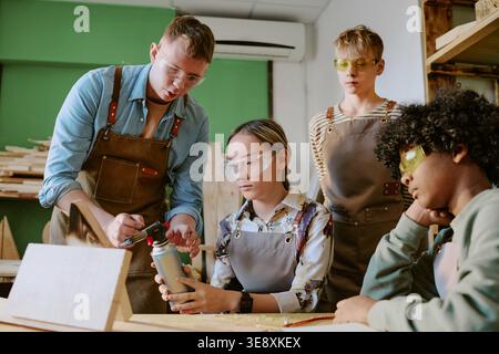 Teenager lernen Holzbearbeitung mit dem Kursleiter in der Schulwerkstatt Stockfoto