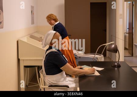 Arnhem, Niederlande - 27. Mai 23: Museumsszene einer Krankenschwester, die an einem Schreibtisch in einem neu gestalteten Gesundheitsraum im Niederländischen Freilichtmuseum in Arnheim schreibt Stockfoto