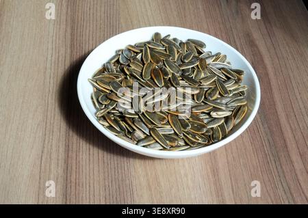 Sonnenblumenkerne in einer weißen Schüssel auf hölzernem Hintergrund. Sonnenblumenkerne. Stockfoto