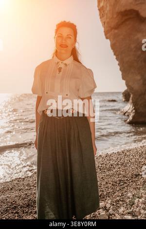 Frau Strandurlaub posiert an einem steinigen Mittelmeerküste während der goldenen Stunde Sonnenuntergang für eine ruhige Lifestyle-Ästhetik Stockfoto