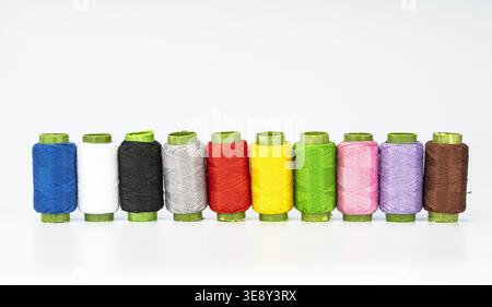 Zehn bunte Fadenspulen, die ordentlich in einer geraden Linie angeordnet sind, mit leuchtendem Blau, weiß, Schwarz, Grau, rot, gelb, hellgrün, rosa, p Stockfoto