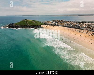 Blick von der Drohne auf Porthmeor Beach und die Landzunge der Insel in St Ives, Cornwall, mit Atlantik-Surf und Strandbesuchern an einem Sommertag, England, Großbritannien. Stockfoto