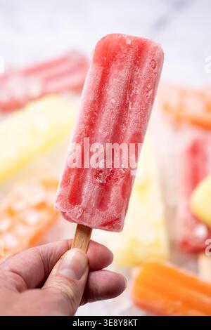 Hand hält rotes Eis auf buntem Eis Hintergrund Stockfoto