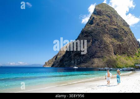 Ein Paar genießt einen gemütlichen Spaziergang entlang des atemberaubenden Strandes in Saint Lucia, umgeben von den majestätischen Pitons vor einem klaren blauen Himmel. Perfekt für einen traumhaften Kurzurlaub und Abenteuer. Stockfoto