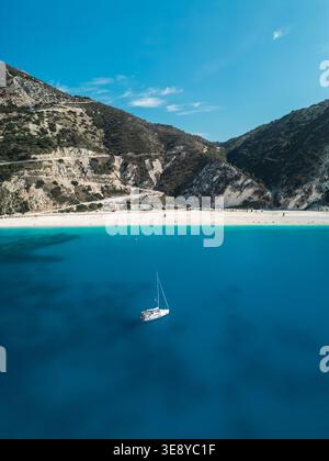 Blick von der Drohne auf Myrtos Beach, Kefalonia, Griechenland, mit einem einsamen Segelboot auf lebhaftem türkisfarbenem Wasser und dramatischen Kalksteinbergen im Oktober. Stockfoto