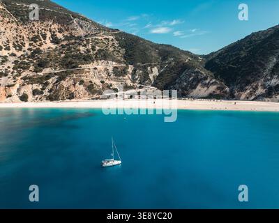 Blick von der Drohne auf Myrtos Beach, Kefalonia, Griechenland, mit einem einsamen Segelboot auf lebhaftem türkisfarbenem Wasser und dramatischen Kalksteinbergen im Oktober. Stockfoto