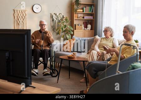 Große Aufnahme von älteren Männern mit Behinderung und älteren Frauen, die im Pflegeheim fernschauen und gemeinsame Freizeit verbringen Stockfoto