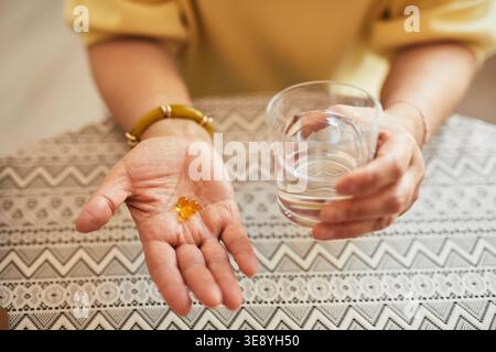 Nahaufnahme einer Seniorin, die Supplementkapseln und ein Glas Wasser hält, tägliche Medikamente im Pflegeheim einnimmt Stockfoto
