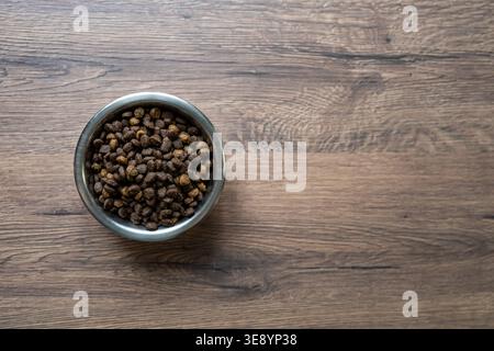 Trockenfutter für Katzen in Metallschale auf Holzhintergrund, Draufsicht minimale Zusammensetzung, Fütterung und Haustierpflegekonzept mit Kopierraum für Branding Stockfoto