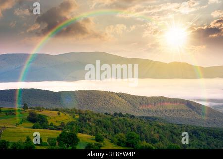 Sonnenuntergang über bergigen ländlichen Gebieten im Frühling. Abgelegene Berglandschaft mit waldreichen Hügeln. Wunderbarer nebeliger Ort der alpinen Landsi Stockfoto