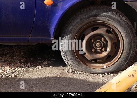 Reifenpanne an einem geparkten blauen Auto in der Nähe von Bordsteinkante, beschädigtes Rad auf Asphalt bei Tageslicht, Problemkonzept am Straßenrand Stockfoto