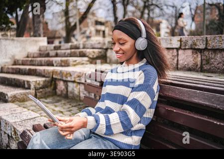 Junge Erwachsene Frau, die draußen Musik mit Kopfhörern und Tablet hört Stockfoto