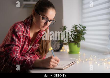 Frau in Brille mit Bleistift schreibt Notizen auf Notizbuch zu Hause. journal Stockfoto