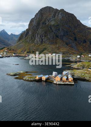Blick aus der Vogelperspektive auf die Lofoten mit traditionellen gelben Holzhäusern auf einer felsigen Insel, umgeben von dunklem Meerwasser und steilen Bergen in Nordland, Norw Stockfoto