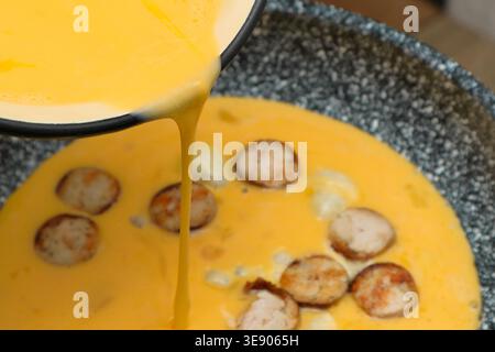 Omelette mit Wurst kochen. Flüssiges Ei für Rührei mit wird in die Pfanne gegossen. Stockfoto