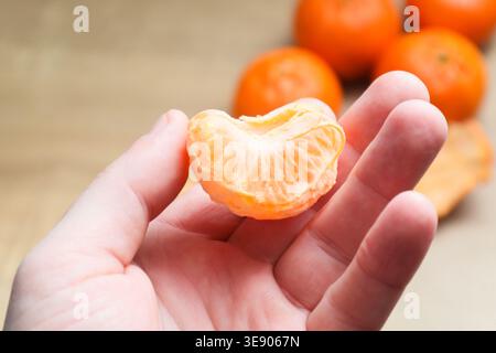 Mann mit Mandarinenscheiben am Tisch drinnen. Nahaufnahme von leckeren gesunden Mandarinenfrüchten. Blick von oben. Makroaufnahme eines Mannes, der leuchtend orange Tangeri hält Stockfoto