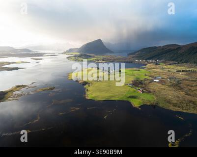 Aus der Vogelperspektive der Lofoten mit grünen Feldern und dramatischen Berggipfeln unter bewölktem Himmel in Nordland, Norwegen. Stockfoto